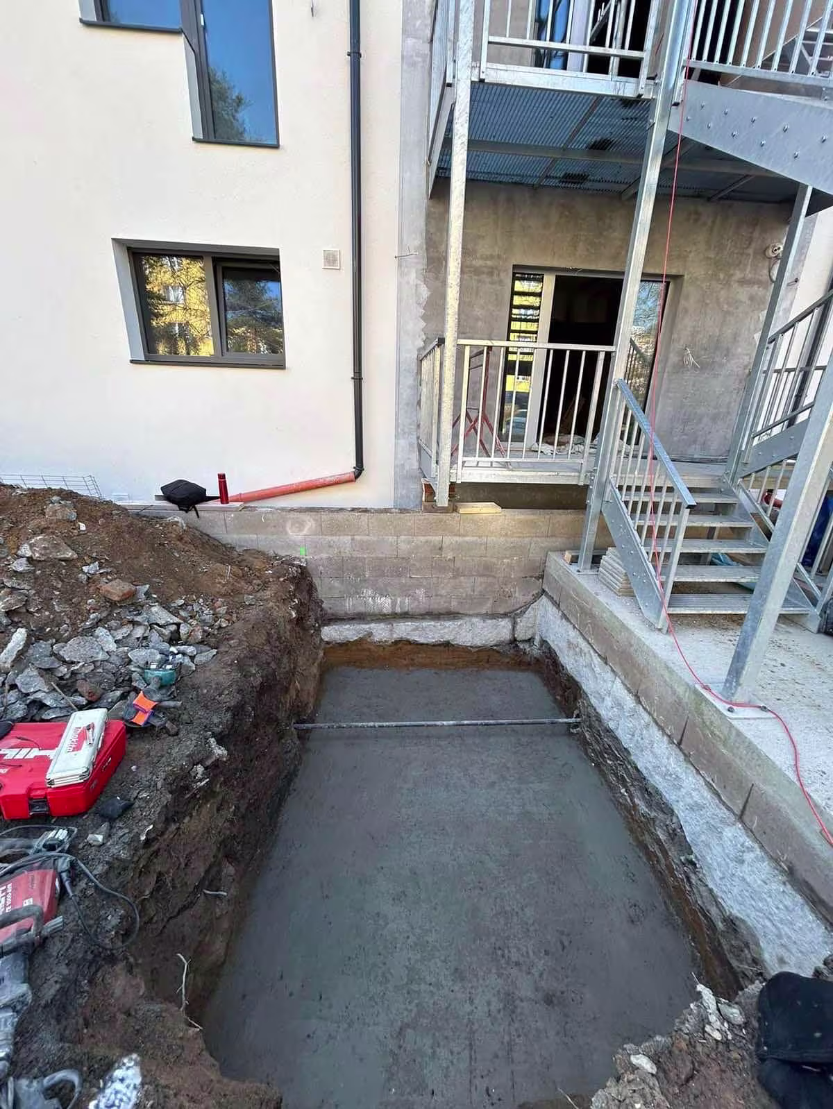 Čerstvě zalitá betonová základová deska (podkladní beton) na dně výkopu pro výtahovou šachtu.