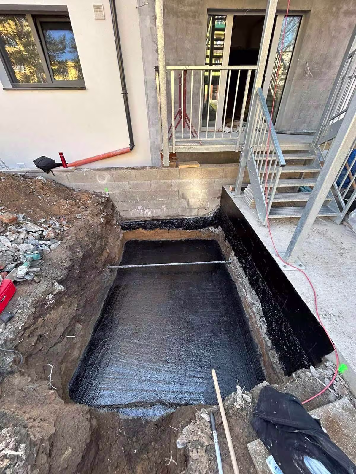 Aplikace černé hydroizolační stěrky na betonové stěny základů výtahové šachty.