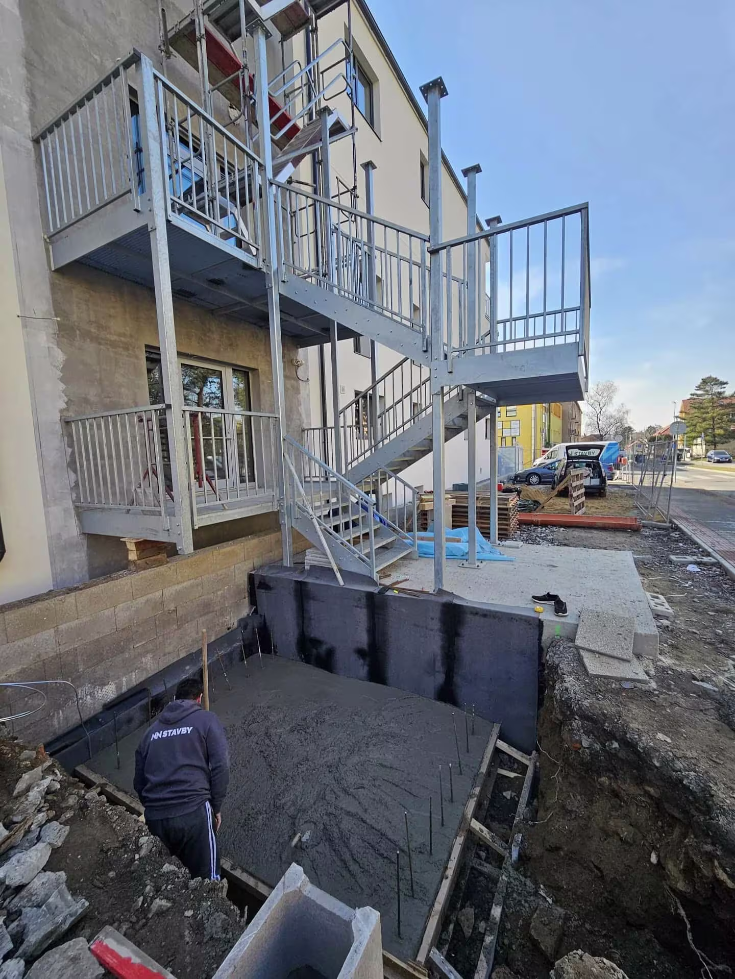 Proces lití betonu do připravených základů u ocelové konstrukce schodiště.