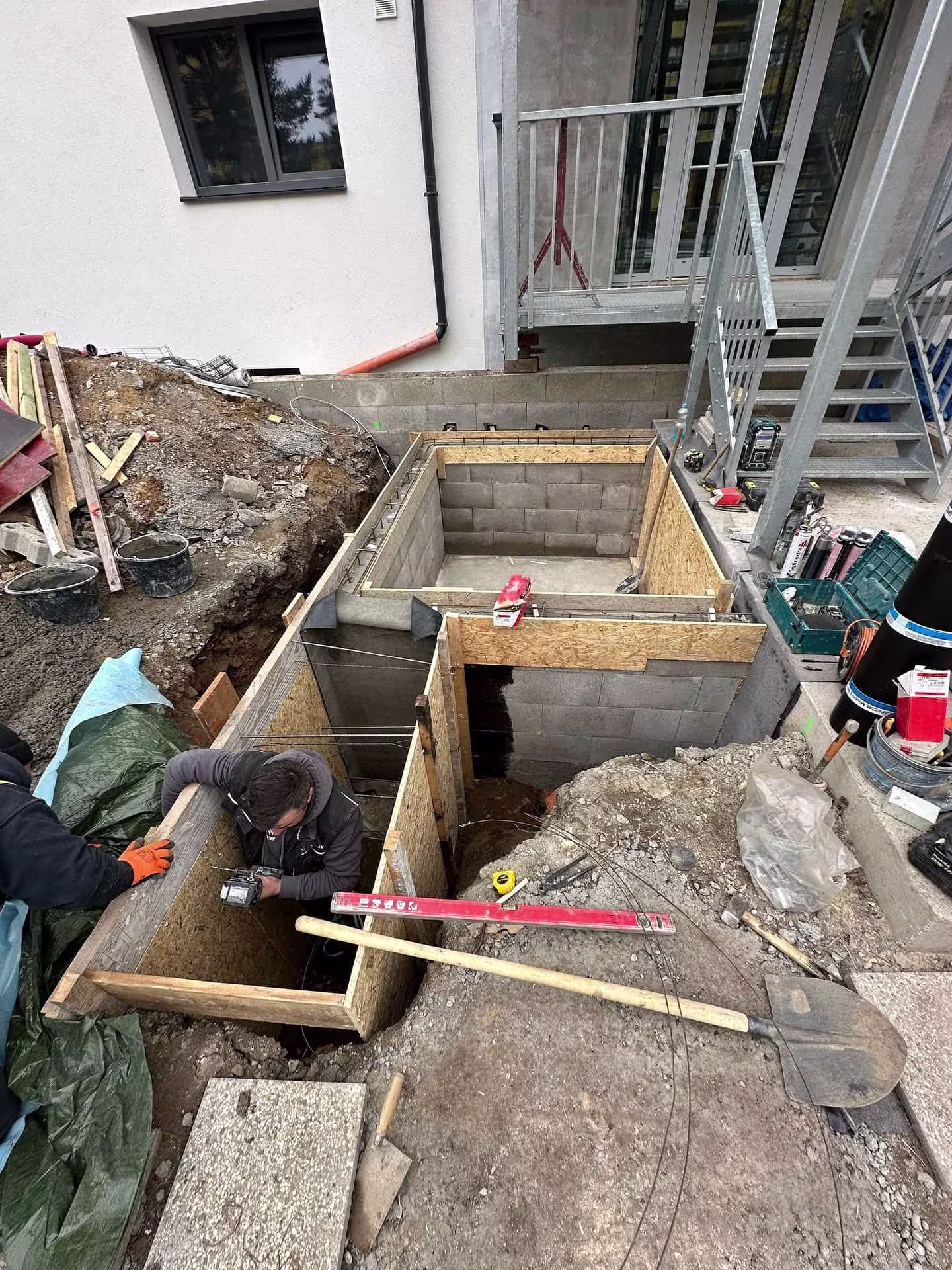 Dva pracovníci montují bednění a připravují základy pro novou výtahovou šachtu v Hloubětíně.