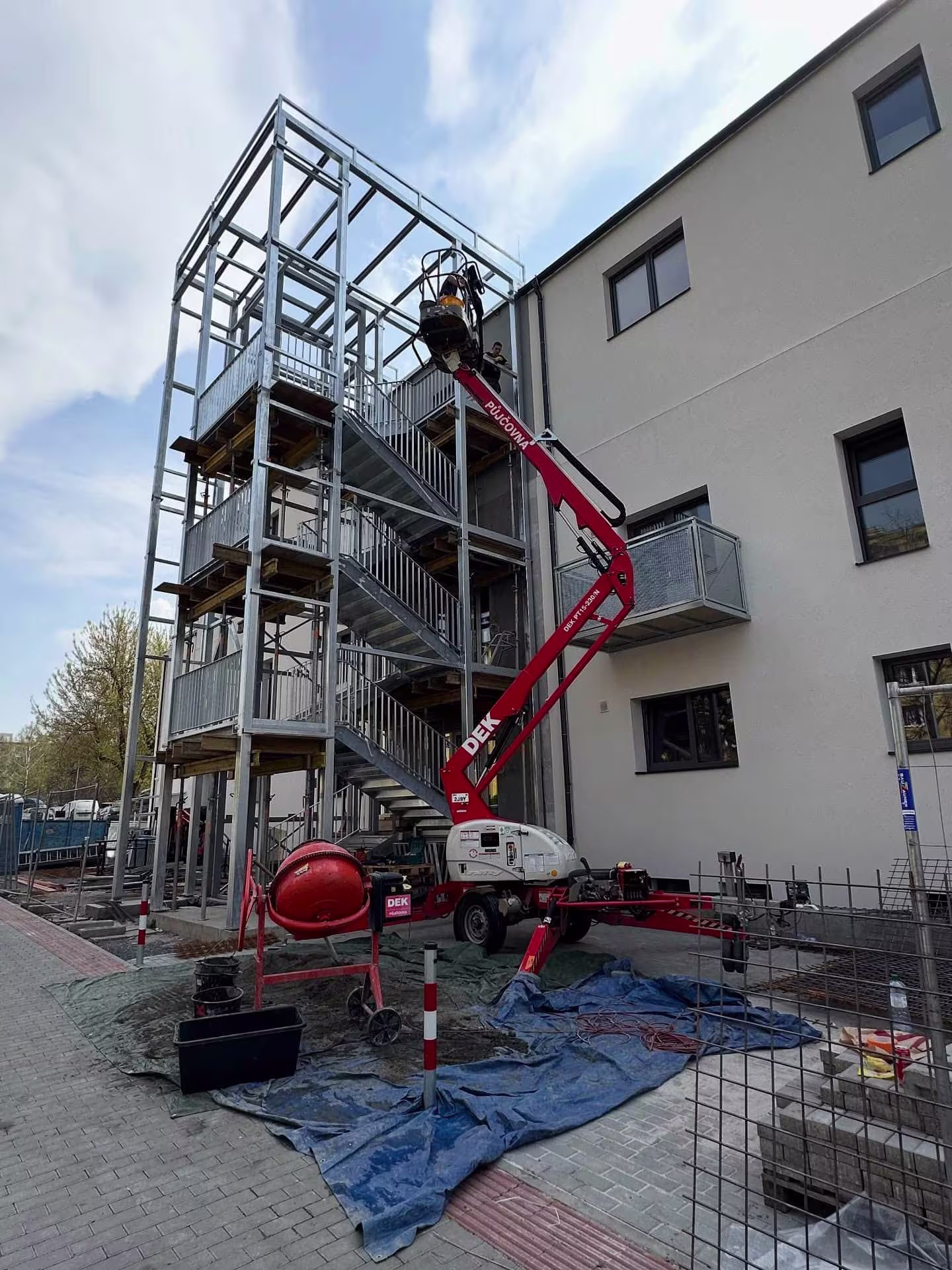 Pracovník na vysokozdvižné plošině provádí montáž horních pater ocelové konstrukce výtahové šachty.