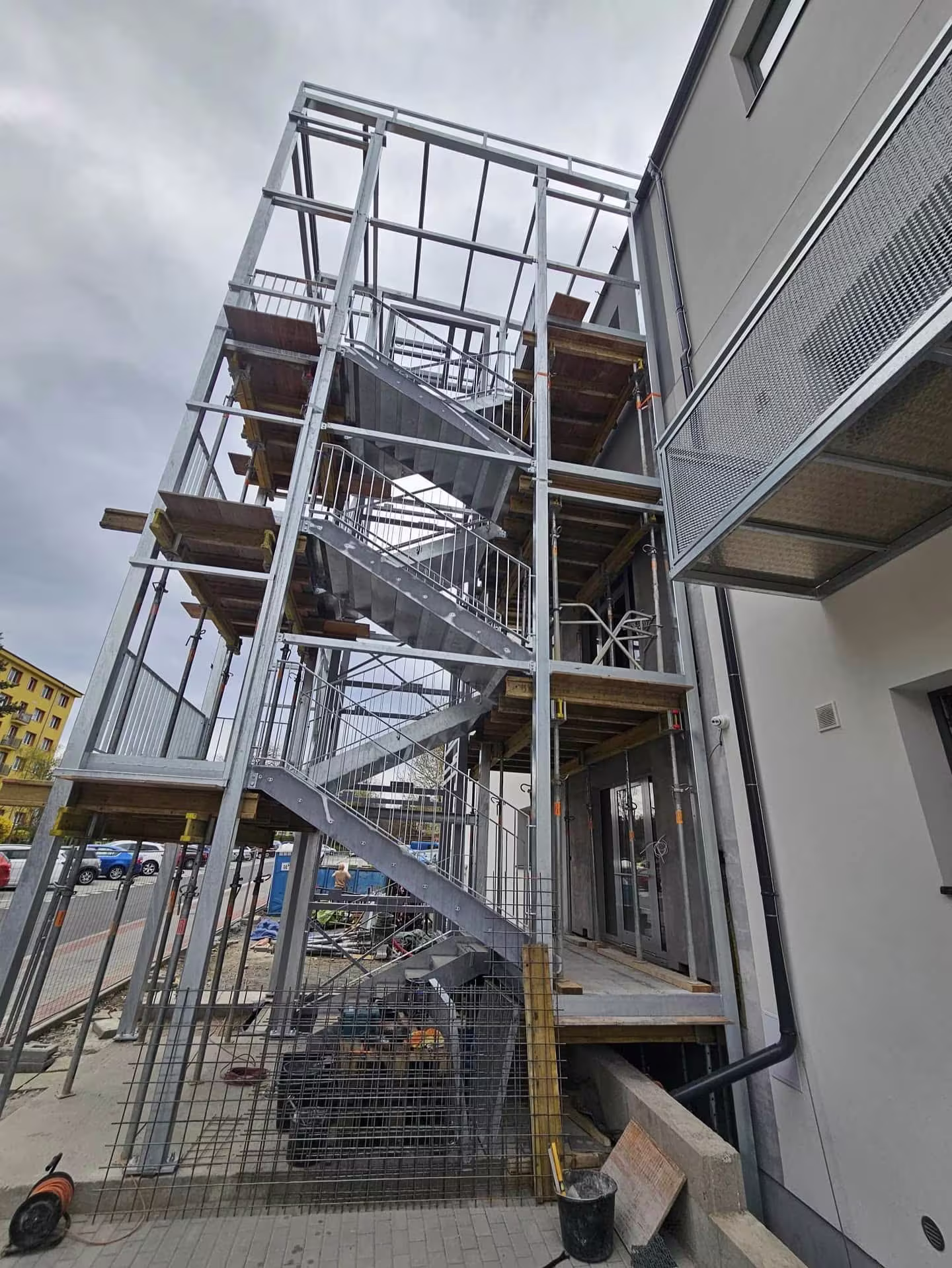 Pohled zespodu na nosnou ocelovou konstrukci a betonovou podestu propojující výtah s budovou.