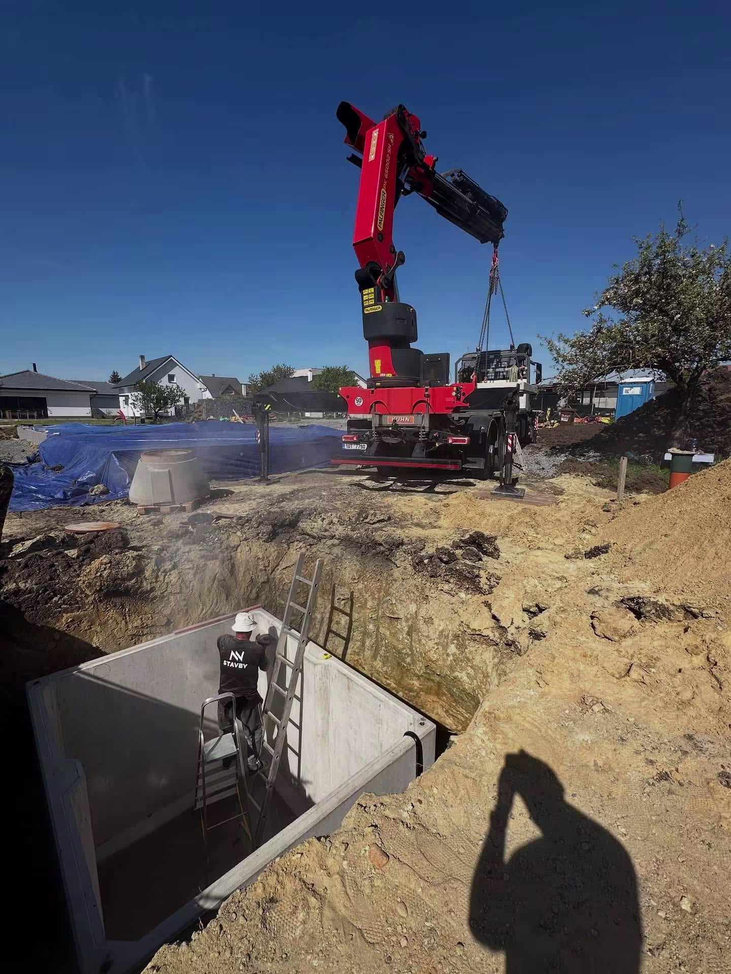 Jeřáb opatrně spouští betonovou jímku do připraveného výkopu během realizace v Čakovicích.